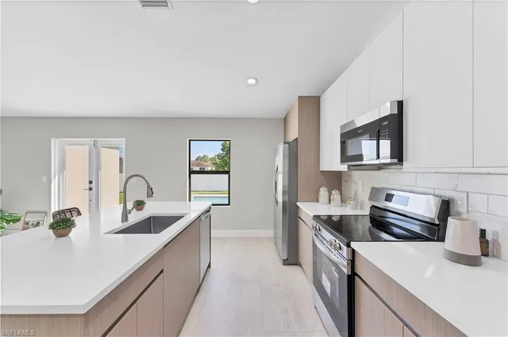 Kitchen featuring flat-panel cabinetry, a spacious island with a single-basin undermount sink, quartz countertops, and a white subway tile backsplash
