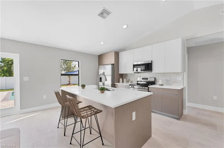 Kitchen featuring a central island with a quartz countertop, white upper cabinetry, wood-finish lower cabinetry, and stainless steel appliances