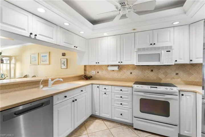Updated kitchen with plenty of white cabinetry, recessed lighting, detailed ceiling, tumbled marble backsplash.