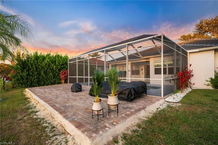Rear view of property with a lanai, a sunroom, a patio area, a lawn, and stucco siding