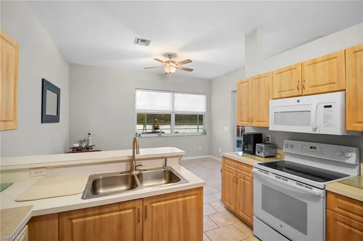 Kitchen featuring white appliances, light countertops, light tile patterned floors, ceiling fan, and light wood finish cabinets