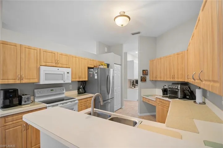 Kitchen with white appliances, light countertops, light wood finish cabinetry, and a peninsula