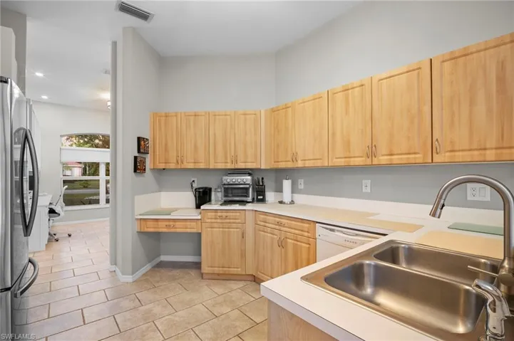 Kitchen with light wood finish cabinets, freestanding refrigerator, light countertops, light tile patterned floors, and white dishwasher