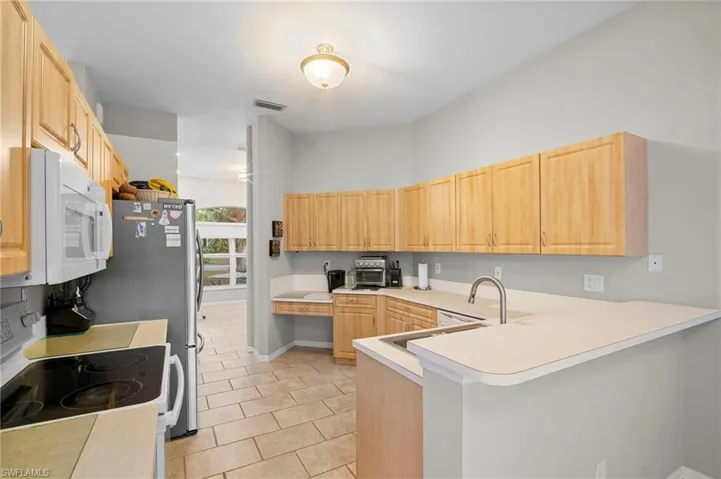 Kitchen featuring white appliances, light countertops, a peninsula, light wood finish cabinets, and light tile patterned flooring