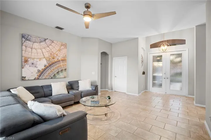 Living area with french doors, a ceiling fan, arched walkways, and light tile patterned floors