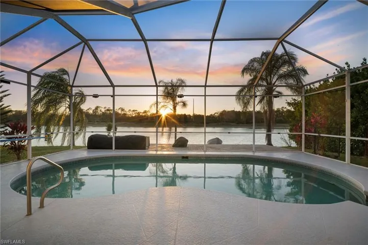 Pool at dusk featuring an outdoor pool, a sunroom, and a water view