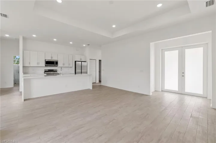 Unfurnished living room with a raised ceiling, light hardwood / wood-style flooring, and french doors