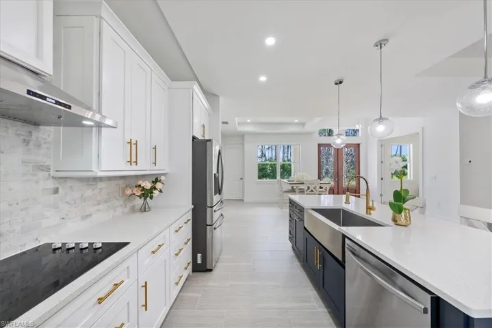 Kitchen with white cabinets, range hood, stainless steel appliances, decorative backsplash, and pendant lighting