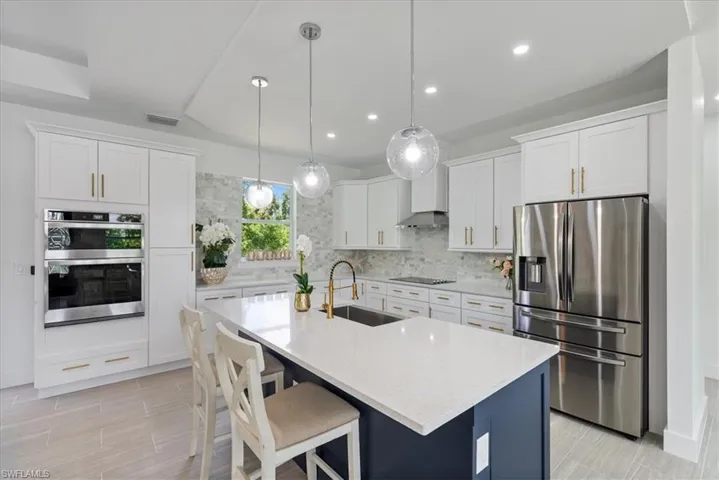 Kitchen with wall chimney range hood, stainless steel appliances, white cabinets, sink, and backsplash
