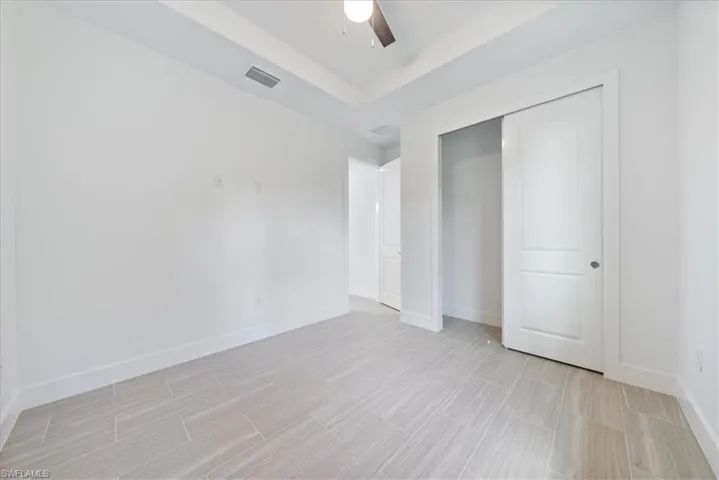 Unfurnished bedroom with a tray ceiling, ceiling fan, and a closet