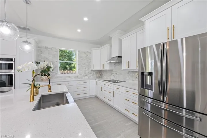Kitchen with stainless steel appliances, wall chimney range hood, sink, light stone counters, and decorative backsplash