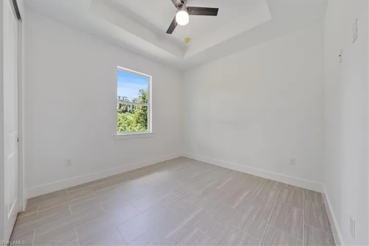 Unfurnished room featuring a raised ceiling, light tile patterned floors, and ceiling fan