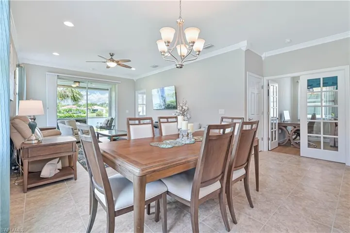 Tiled dining room with ceiling fan with notable chandelier and crown molding