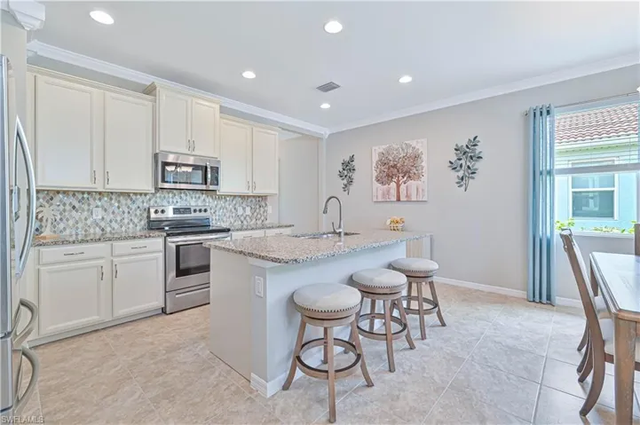 Kitchen with stainless steel appliances, ornamental molding, sink, light stone counters, and light tile patterned floors