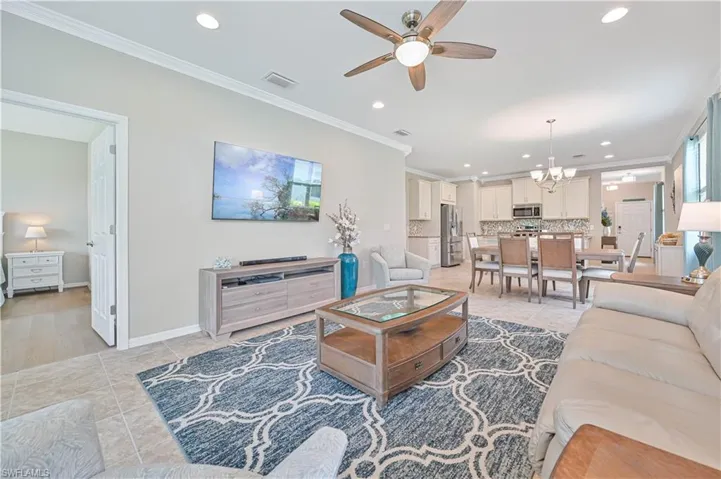 Living room with ceiling fan with notable chandelier, ornamental molding, and light tile patterned floors