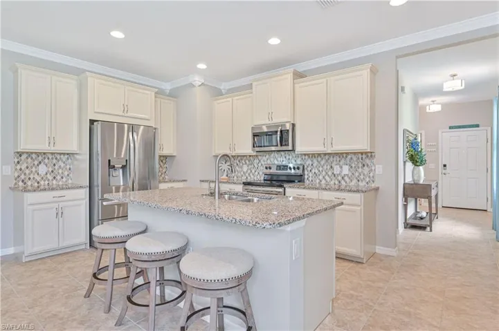 Kitchen with appliances with stainless steel finishes, light tile patterned flooring, decorative backsplash, and light stone countertops