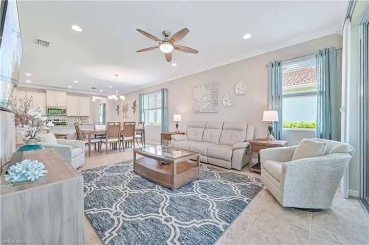 Living room featuring light tile patterned flooring, ceiling fan with notable chandelier, and crown molding