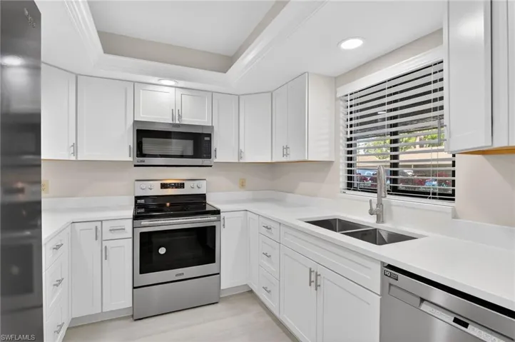 Kitchen featuring stainless steel appliances, white cabinets, light stone counters, recessed lighting, and a tray ceiling