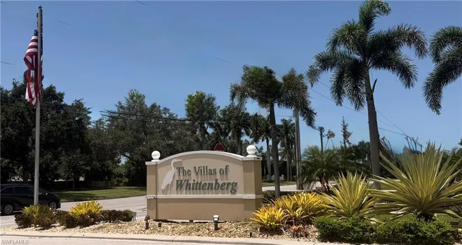 Monument sign featuring "The Villas of Whittenberg" text, flanked by mature palm trees and lush, diverse landscaping