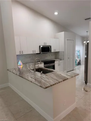 Kitchen featuring a peninsula with a patterned countertop and undermount sink, white cabinetry, stainless steel appliances, and a tiled backsplash