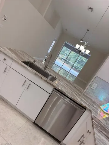 Kitchen featuring a stainless steel undermount sink, a stainless steel dishwasher, white flat-panel cabinetry with brushed nickel hardware, and a variegated stone countertop