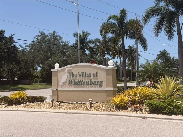 The Villas of Wittenberg entrance sign featuring a heron emblem, set against a background of established palm trees and varied foliage