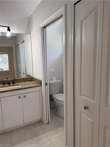 EnSuite Bath with water closet which has pocket door for privacy. Earth Tone colored Granite countertop, white cabinetry with silver hardware, and a large wall-mounted mirror, tile flooring. CLosets left and right before entering En Suite Bath.