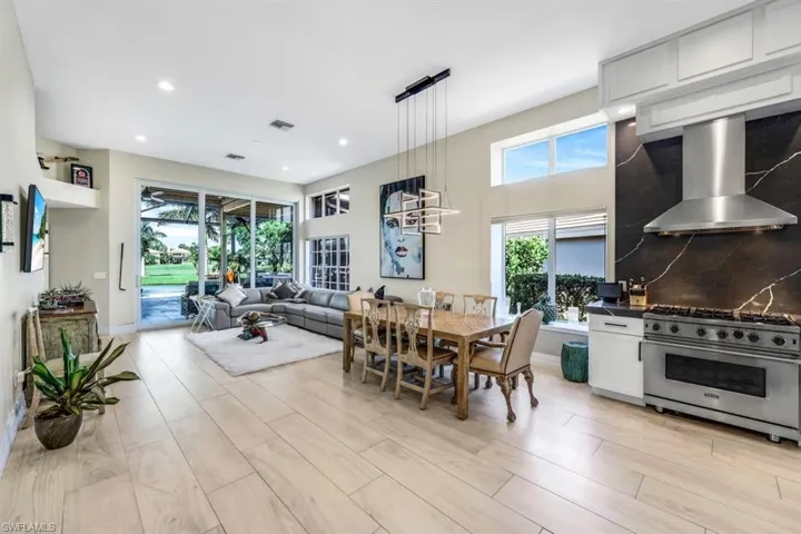Kitchen featuring wall chimney exhaust hood, light hardwood / wood-style floors, hanging light fixtures, white cabinetry, and high end range