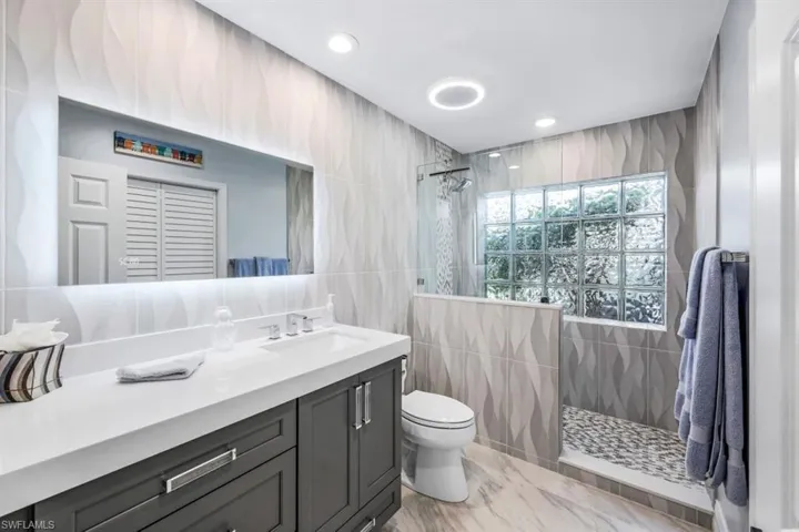 Bathroom featuring tiled shower, toilet, tile walls, and vanity