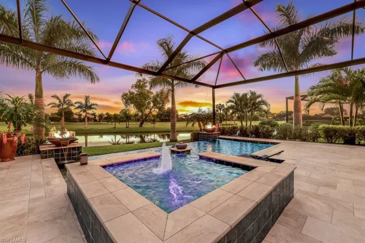 Pool at dusk featuring a water view, a lanai, a patio, and an in ground hot tub