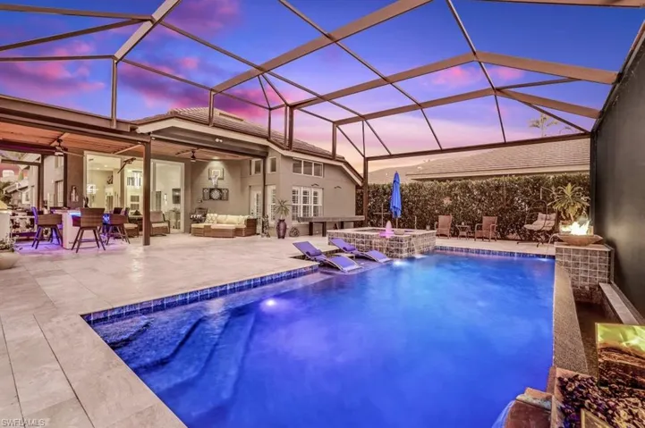 Pool at dusk featuring glass enclosure, pool water feature, outdoor lounge area, ceiling fan, and a patio