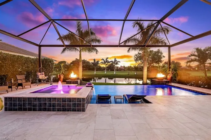 Pool at dusk featuring glass enclosure, a water view, a patio, and pool water feature
