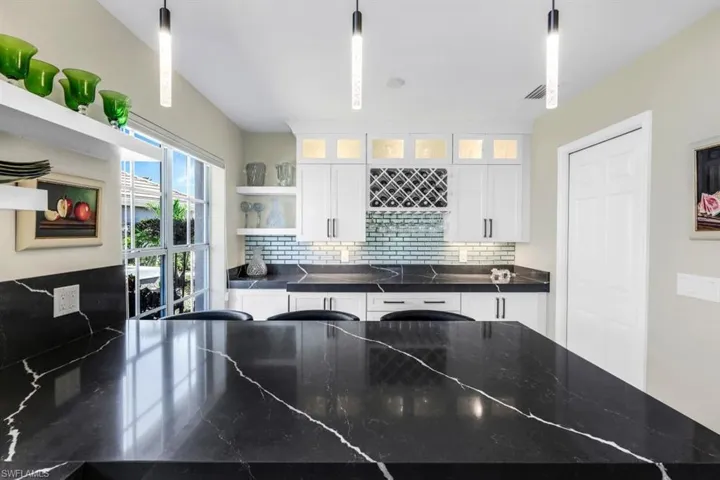 Kitchen with white cabinets, hanging light fixtures, and tasteful backsplash