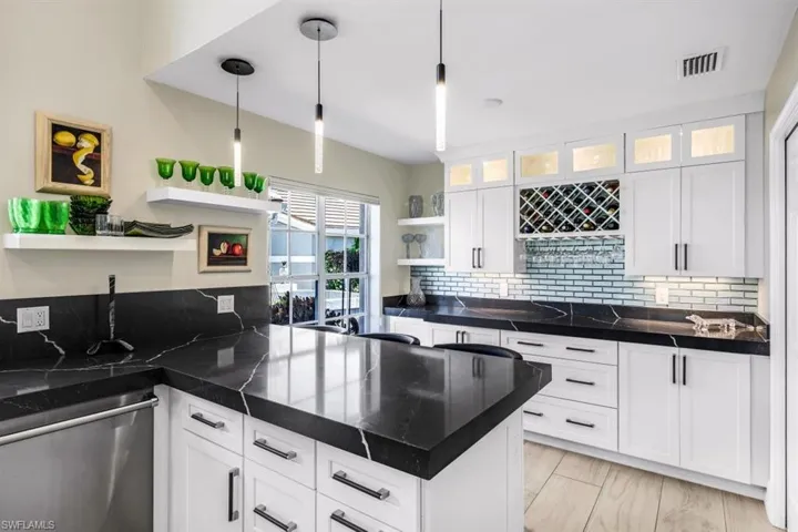 Kitchen with white cabinetry, backsplash, stainless steel dishwasher, and hanging light fixtures