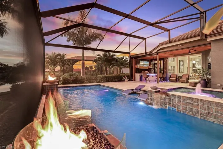 Pool at dusk with a lanai, an in ground hot tub, pool water feature, ceiling fan, and a patio
