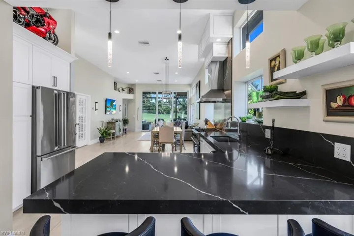 Kitchen featuring decorative light fixtures, high end refrigerator, a kitchen bar, sink, and white cabinets