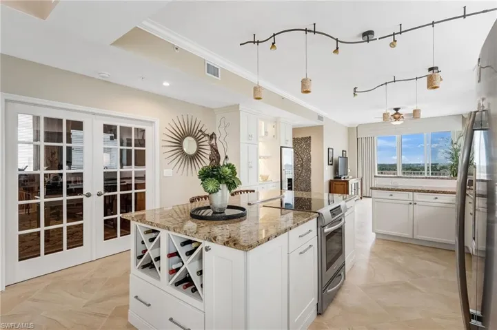 Glass French doors create a bright, private office or den, while the kitchen dazzles as a chef’s haven, boasting a massive island, Level 3 granite countertops, stainless steel appliances, a built-in wine rack, and elegant white cabinetry.