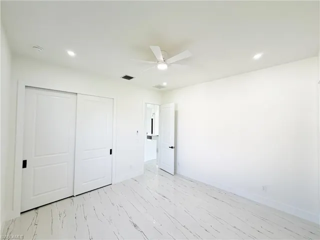 Interior room featuring white walls, large format tile flooring with dark veining, recessed lighting, and a ceiling fan