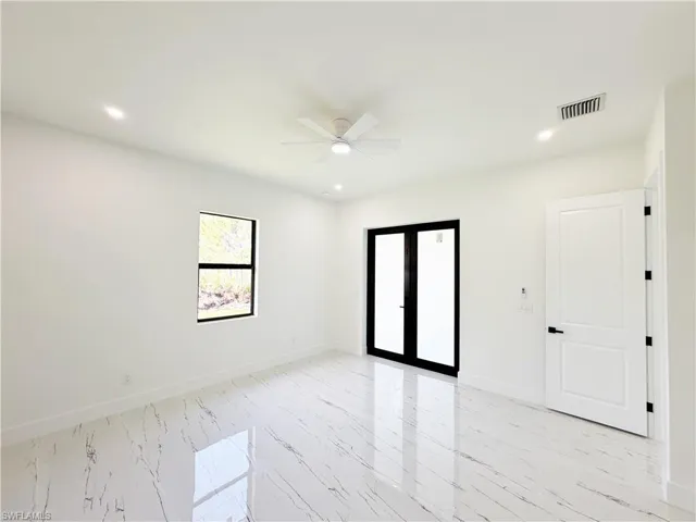Spacious room featuring large format white tile flooring with black veining, white walls, and a contemporary ceiling fan