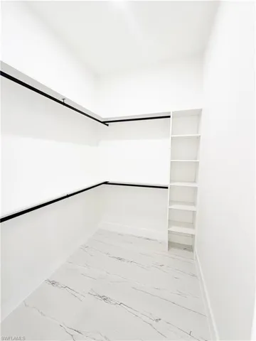 Walk-in closet featuring white walls, black garment rods, built-in shelving, and marble-look tile flooring