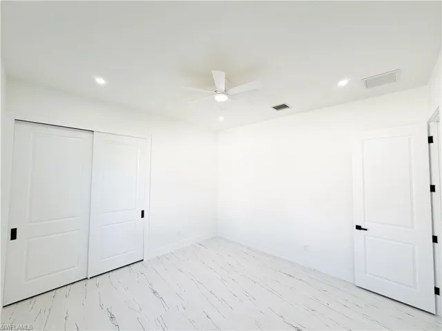 Bright interior space featuring wood-finish flooring with a white marble-look, a white ceiling fan, recessed lighting, white interior doors, and black hardware
