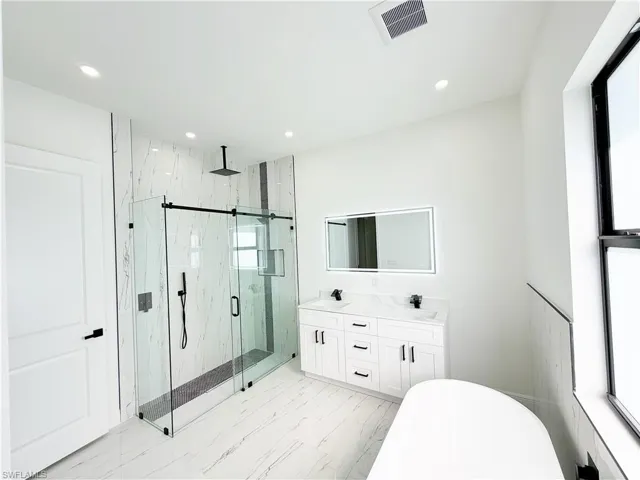Spacious bathroom featuring a glass-enclosed shower with a rainfall showerhead, dual vanity with undermount sinks, illuminated mirror, and a freestanding soaking tub