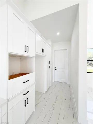 Hallway featuring white shaker cabinetry, black hardware, and stone-look flooring