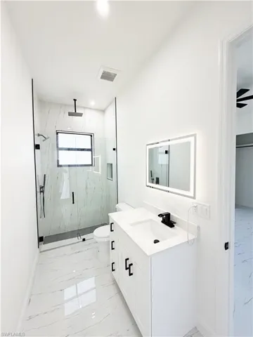 Contemporary bathroom featuring large format floor and shower wall tile, a frameless glass shower enclosure with matte black fixtures, and a vanity with an integrated sink and illuminated mirror