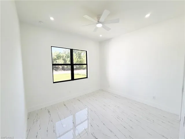 Bright interior room featuring a large window with black framing, white walls, and white flooring with dark veining