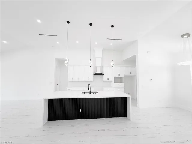 Open-concept kitchen featuring a waterfall island with a fluted black base, white cabinetry, integrated range hood, and pendant lighting