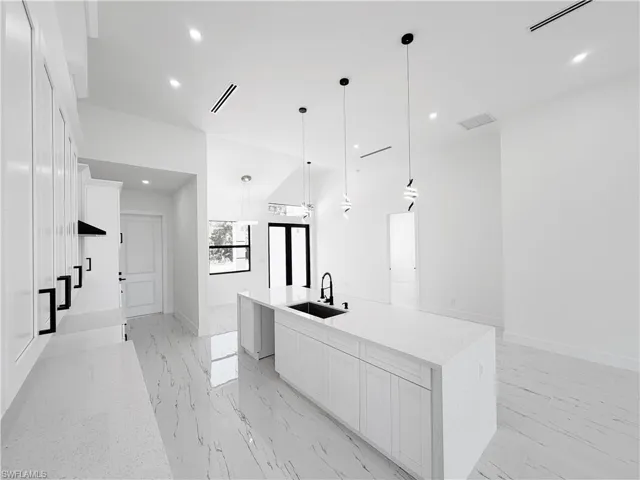 Open-concept kitchen featuring a waterfall island with integrated sink, pendant lighting, recessed lighting, and white cabinetry