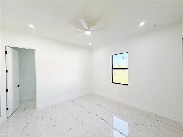 Spacious interior room featuring white walls, large format tile flooring with dark veining, a ceiling fan, and recessed lighting