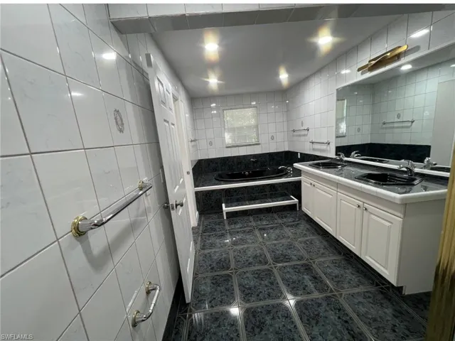 Full bath with tile walls, dark tile patterned floors, a bath, and double vanity