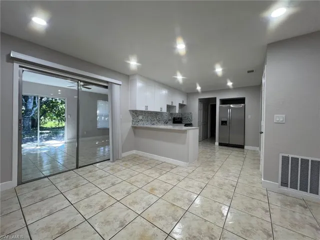 Kitchen featuring white cabinetry, tasteful backsplash, stainless steel refrigerator with ice dispenser, a peninsula, and light tile patterned floors